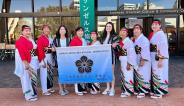 nine women members of the minyo ken kai dance group holding their group banner.